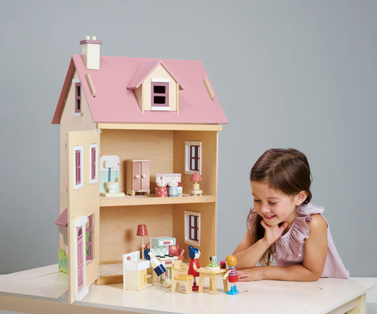 Meisje speelt met een houten poppenhuis met roze dak en poppetjes aan tafel.